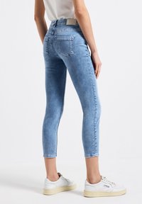 Jeans skinnys de color azul claro con una textura suave, cintura de talle medio y bolsillos traseros. Combinados con zapatillas blancas para un look casual.