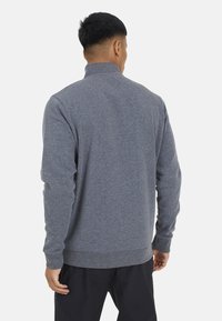 Pullover in pile grigio con colletto alto e polsini e fondo a coste. Il tessuto appare morbido e texturizzato, adatto per un abbigliamento casual.