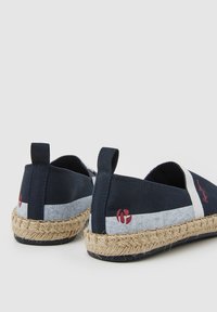 Zapatillas deportivas de algodón azul marino con una banda de textil gris, suela de yute, y un pequeño detalle de logo rojo cerca del talón. Diseño de punta redonda.