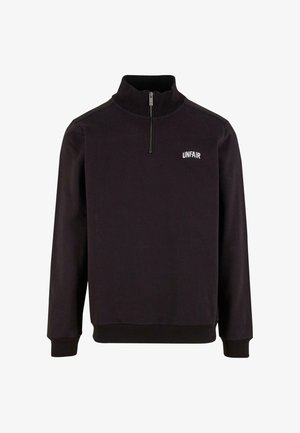 Čierna mikina so štvrťzipovým golierom, rebrovanými manžetami a lemom, so slovom "UNFAIR" vyšitým bielou farbou na ľavej hrudi. Mäkka textúra látky.
