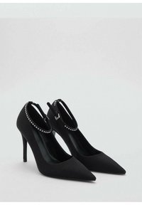 Chaussures noires à talons hauts avec un bout pointu, présentant une finition satinée et une bride de cheville ornée de strass.