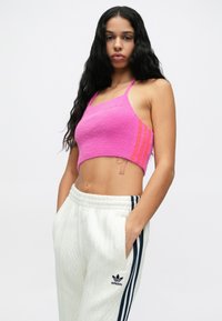 Ροζ κοντό πλεκτό τοπ με λεπτές τιράντες και υφή, σε συνδυασμό με λευκή υφασμάτινη φόρμα με μαύρες ρίγες και λογότυπο.