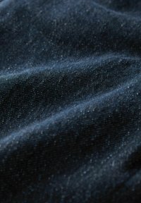 Sötét farmeranyag, amely texturált felületet mutat finom pettyekkel, gazdag kék árnyalattal és puha eséssel.