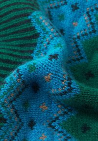 Strickstoff mit einer lebhaften blauen Basis und grünen Akzenten, geometrischen Mustern sowie kleinen braunen und schwarzen Motiven; weiches und strukturiertes Erscheinungsbild.