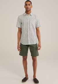 Rövidujjú ing geometrikus mintával fehér és sötétkék színben, olívazöld rövidnadrággal és fonott fekete espadrille-lal párosítva.