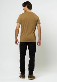 Herre kortermet t-skjorte i beige bomull, med runda hals. Båret med svarte jeans og brune snøresko, vist fra bak.