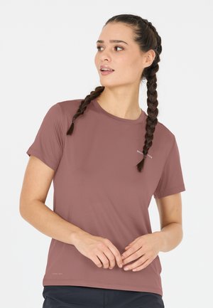 Vrouw met gevlochten haar in een mauve sporttop met korte mouwen, die met haar handen losjes voor zich uit kijkt.