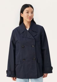 Marineblå dobbeltknappet jakke lavet af letvægtsstof, med store knapper, en bred krave og sidelommer.