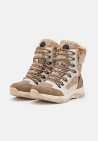 Bottes beiges avec tige synthétique matelassée, accents en daim marron, bordure en fausse fourrure et semelle en caoutchouc texturé. Elles présentent des lacets tressés et des œillets en métal.
