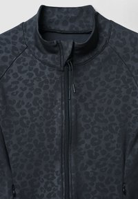 Giacca nera con zip caratterizzata da un sottile motivo a leopardo. Tessuto strutturato con alto colletto e dettaglio della zip.