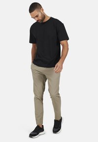 Czarna bawełniana koszulka zestawiona z teksturowanymi beżowymi spodniami i czarnymi sneakersami, o dopasowanym kroju i krótkich rękawach.