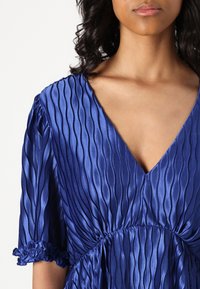 Purple satin dress featuring a V-neck, pleated texture, and short ruffled sleeves, creating a flowy silhouette.