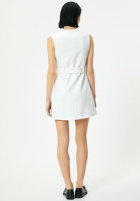 Vestido blanco ajustado con un diseño sin mangas, cintura ceñida y una textura suave, complementado por un cinturón ancho en la espalda.