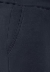 Mörkblå sweatpants med en slät textur, med sidofickor och sömmar som ger hållbarhet. Tyget verkar lätt och flexibelt.