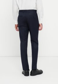 Pantaloni bleumarin, cu o croială adaptată, două buzunare la spate și o textură netedă. Purtați cu o cămașă albă și pantofi negri.
