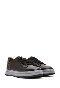Zapatillas de cuero negro con una textura suave, puntera redonda, cordones planos y una suela de goma translúcida en contraste. Diseño minimalista sin patrones.