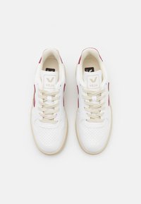 Sneakers in pelle bianca con accenti laterali bordeaux, punta perforata, lacci crema e suola in gomma beige. Logo del marchio sulla linguetta.