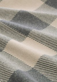 Wollen deken met een geruit patroon in grijs en crème. De stof heeft een zachte textuur met uitgesproken diagonale strepen.