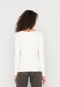 Top bianco a maniche lunghe con scollo a scallop, design aderente e texture morbida, abbinato a pantaloni in denim grigio scuro.