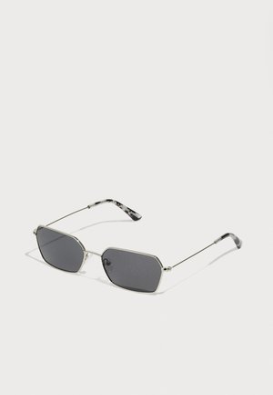 Gafas de sol metálicas de color plateado con lentes oscuros. Montura hexagonal con brazos finos que presentan un patrón veteado. Diseño ligero.