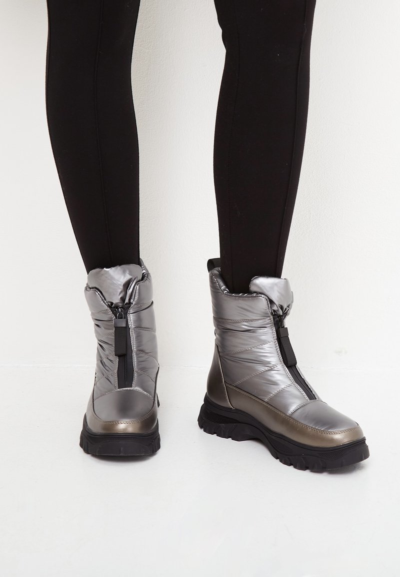 Bottes de cheville rembourrées argent métallisé avec une fermeture éclair sur le côté, semelles noires épaisses et un design froncé, présentant des matériaux lisses et texturés.