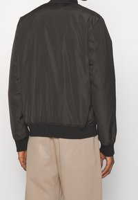 Svart vadderad bomberjacka med elastiska ärmslut och midja, slät yta och minimalistisk design, med uppstående krage.