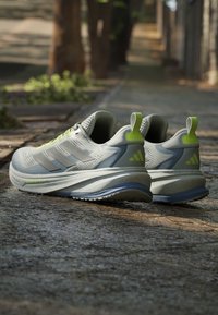 Chaussures de course gris clair avec des touches vert citron reposant sur un chemin extérieur texturé sous une lumière douce.