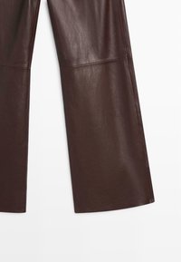 Pantaloni ampi in pelle marrone con una texture liscia, caratterizzati da un taglio dritto e dettagli di cucitura minimi all'orlo e alle cuciture.