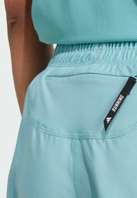 Helle blaue Laufshorts aus einem strukturierten Stoff, mit einem elastischen Bund und einer Gesäßtasche mit einem schwarzen "RUNNING"-Label.