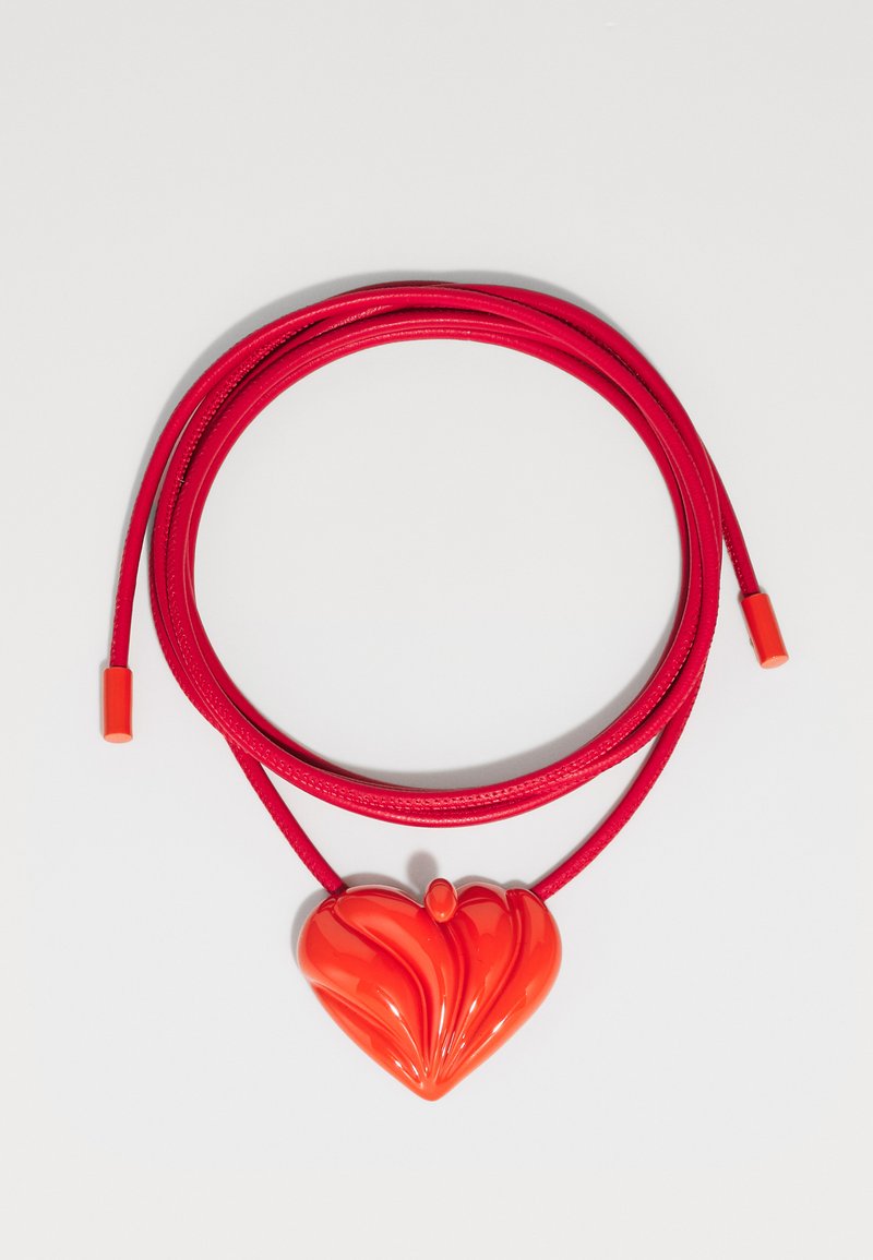 Collar rojo con un colgante en forma de corazón brillante que presenta patrones ondulados, sobre un cordón rojo suave con extremos ajustables.