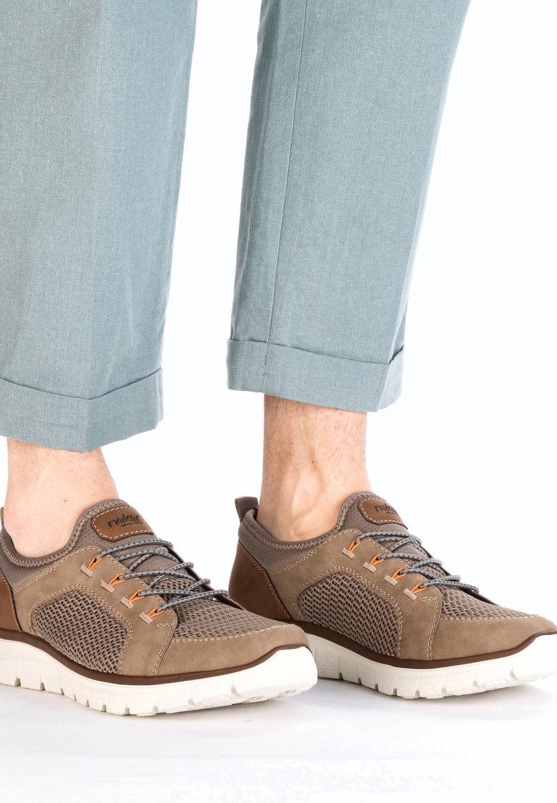 Baskets en maille marron et en daim avec des accents orange, semelle en caoutchouc blanche et lacets gris. Associées à un pantalon léger bleu clair retroussé.