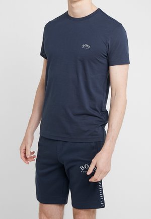 Mand iført navyblå BOSS-branded kortærmet t-shirt og matchende shorts, stående mod en ensfarvet lys baggrund.