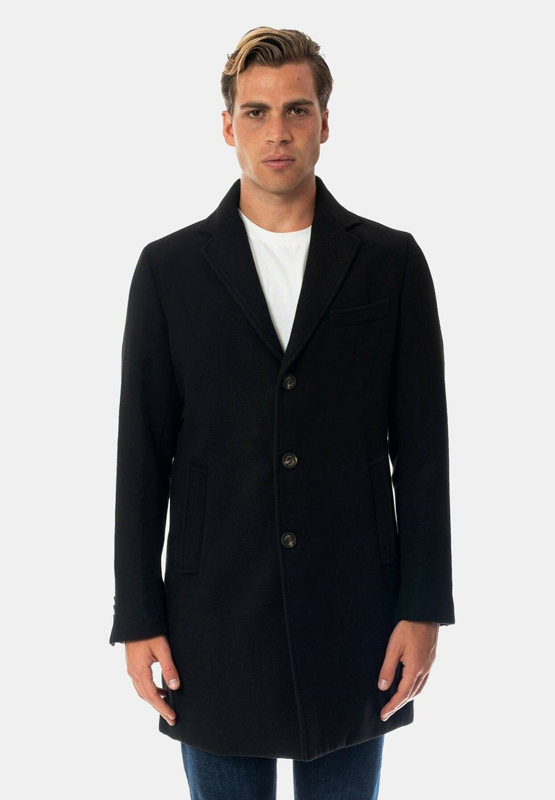 Cappotto in lana nera con silhouette strutturata, design a un bottone, rever a punta, tre bottoni e tasche laterali. Texture liscia.