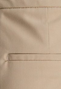 Béžová tkanina s hladkou texturou. Má vodorovný šev a kapsu s lemováním na pravé straně. Viditelný pevný šev.