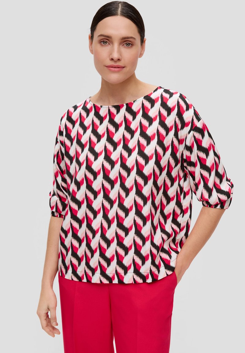 Haut ample en tissu avec un motif en zigzag répétitif dans les tons rose, blanc et noir. Doté d'un col large et de manches roulées.