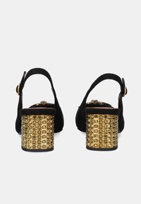 Zapatos slingback de ante negro con tacones de bloque adornados con tachuelas doradas. Los tacones presentan un patrón en cuadrícula de tachuelas redondas para un detalle adicional.