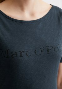 Tummansininen pyöreäkauluksinen t-paita, jossa on hienovarainen, haalistunut painatus "Marc O'Polo" etupuolella. Pehmeää puuvillamateriaalia, jossa on sileä pinta.