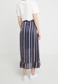 Striped midi skirt in navy and cream, featuring a ruffled hem, sheer texture, and elastic waist, paired with white sneakers.