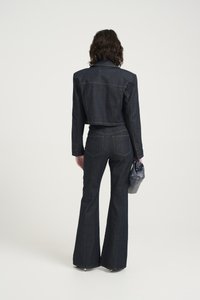 Mørk denim cropped jakke kombinert med flare-bukser. Outfitten har sømdetaljer og en teksturert overflate, supplert med en liten veske.
