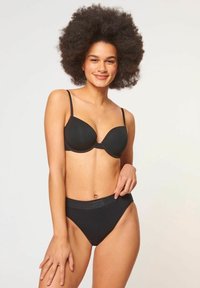 Schwarzer BH mit gepolsterten Cups und verstellbaren Trägern, kombiniert mit hochgeschnittenen schwarzen Panties. Glatte Textur und minimalistisches Design.