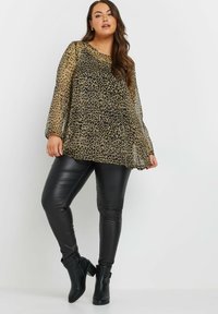 Top trasparente a maniche lunghe con stampa leopardata, beige e nera, abbinato a pantaloni in finta pelle nera aderenti e stivaletti con tacco chunky.