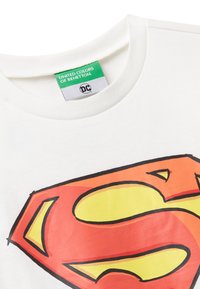 Bílý bavlněný tričko s velkým, vícebarevným logem Supermana v červené a žluté barvě. Zelená etiketa u výstřihu od United Colors of Benetton.
