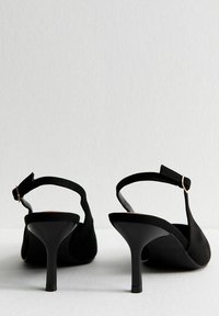 Zapatos de tacón alto negros con acabado de ante, con la parte trasera abierta y correa ajustable. Presentan un tacón elegante y delgado y acentos de diseño mínimos.