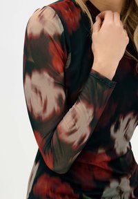 Top de manga larga hecho de una tela ligera y transparente con un patrón floral oscuro en rojos y marrones, que presenta un cuello alto y un diseño ajustado.