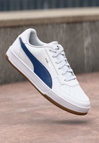 Bijela tenisica s plavom PUMA prugom, teksturirani kožni gornji dio, ravne vezice i perforirani detalji na nožnom prstu; guma potplat.