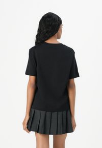 Maglietta nera in cotone a maniche corte, abbinata a una gonna grigia plissettata. Il design presenta un semplice scollo rotondo e una linea dritta.