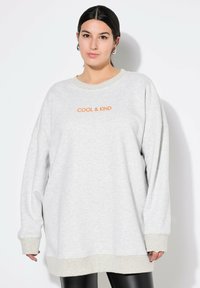 Felpa oversized grigia chiara con la scritta "COOL & KIND" stampata in arancione. Presenta un collo rotondo e polsini a coste, realizzata in tessuto morbido.