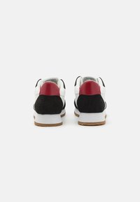 Herresneakers med overdel i svart semsket skinn og hvitt lær, røde hælaksenter og en teksturert gummisåle. Klassisk atletisk design.