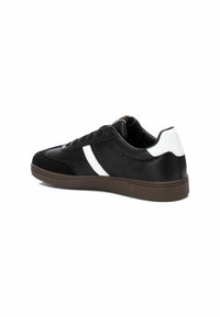 Zapatilla negra con parte superior de cuero liso y detalles en ante. Presenta una franja blanca, un collar acolchado y una suela de goma marrón.