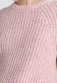 Różowy sweter z dzianiny o prążkowanej fakturze, z okrągłym dekoltem i miękkim, ciepłym wyglądzie z delikatnymi, wielokolorowymi plamkami.